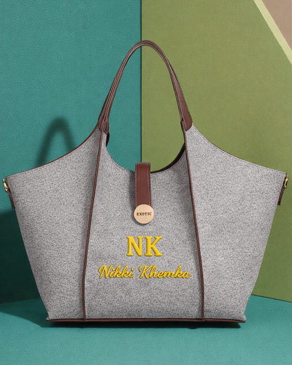 Gray tote bag with brown handles and 'NK Nikki Khanka' embroidery on a green and beige background