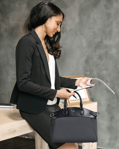 Woman in professional attire holding a black handbag against a gray background