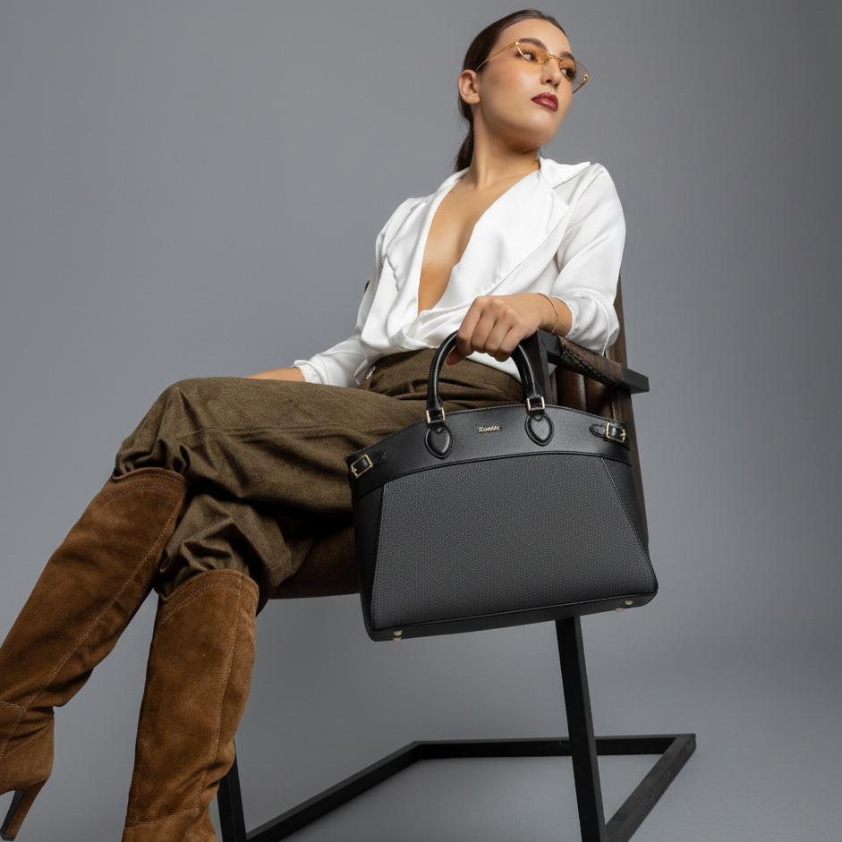 Woman sitting on a chair holding a black handbag against a gray background