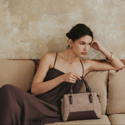Woman sitting on a beige couch holding a handbag against a textured wall.