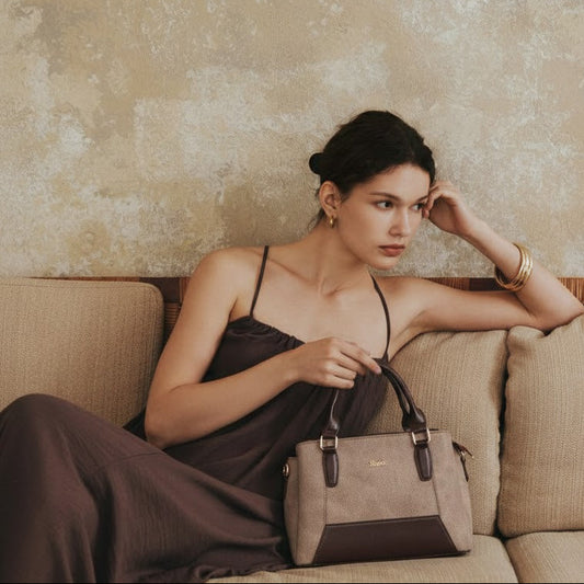 Woman sitting on a beige couch holding a handbag against a textured wall.